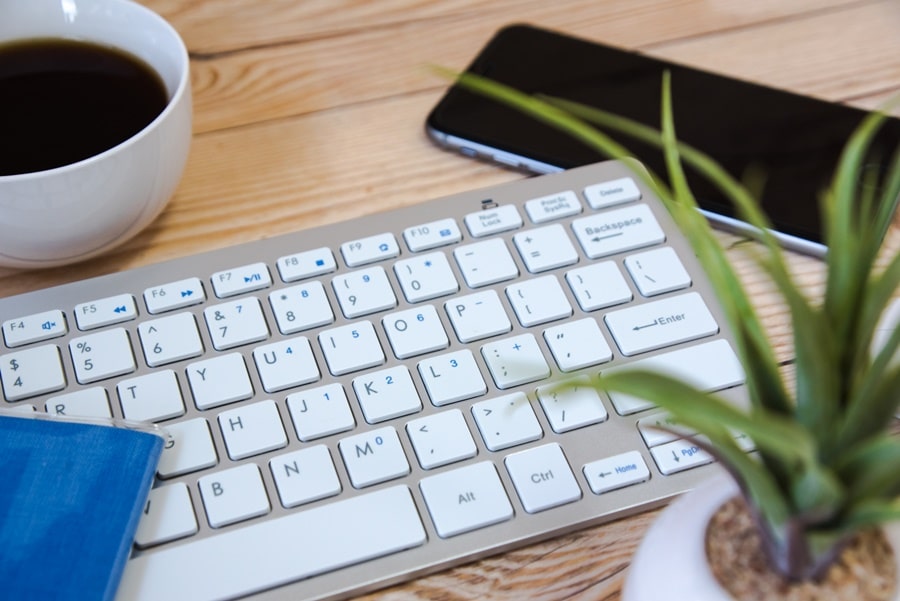 机の上に置いてあるキーボードとコーヒーと観葉植物